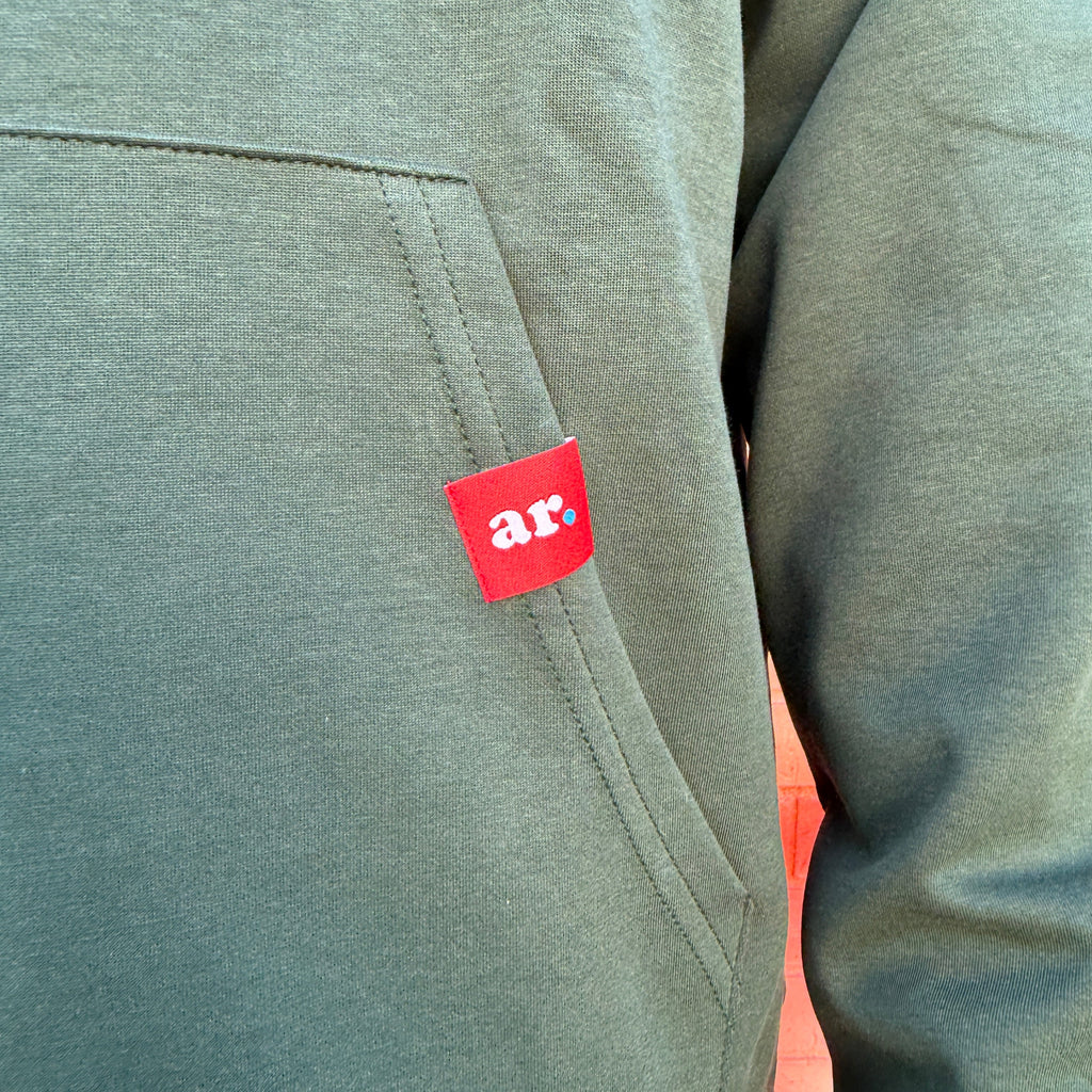 Close-up of a heathered sage green hoodie with a red brand patch featuring the white text 'ar.' on the chest pocket.